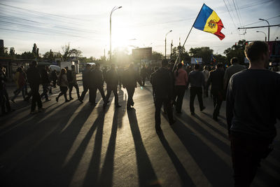 People walking on road against sky during sunset