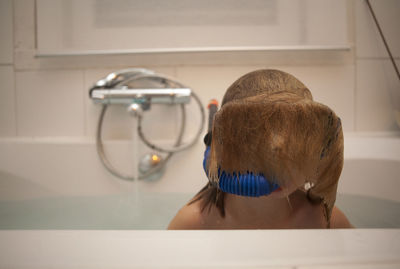 Close-up of teenage girl with wet brown hair covering face in bathtub