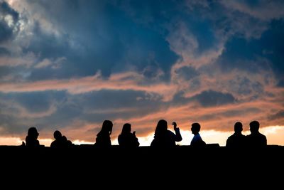 Silhouette people against cloudy sky during sunset