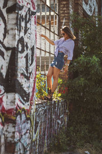 Young woman standing on window sill amidst graffiti wall