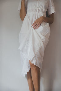 Low section of woman standing against wall wearing a white embroidered dress