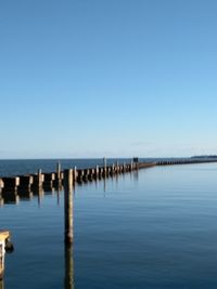 Wooden posts in sea against clear blue sky