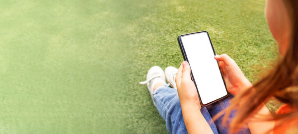 Phone with copy space in the hands of a child close-up on a background of green grass