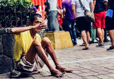 Full length of beggar hiding face while sitting on footpath