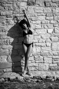 Young woman standing in bikini against stone wall