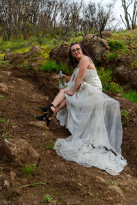 Portrait of young woman in wedding dress sitting on muddy road