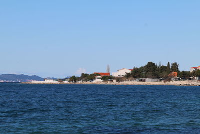 Sea by buildings against clear blue sky