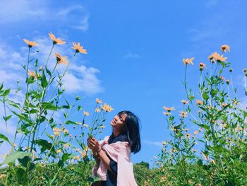 Woman standing by flowering plants against sky