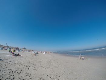 Group of people on beach against clear blue sky