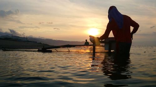 Rear view of man fishing in lake against sky during sunset