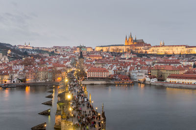 Illuminated buildings by river against sky in city