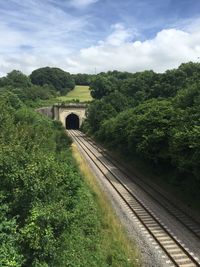 High angle view of railroad tracks leading towards tunnel amidst trees against sky