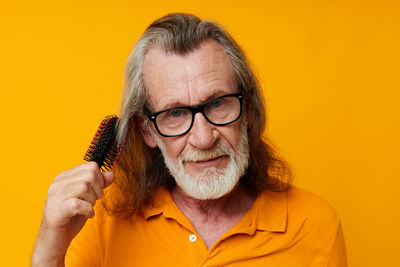 Senior man combing hair against yellow background