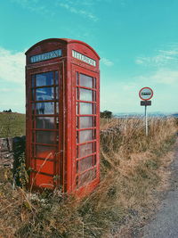 Red telephone booth on road against sky