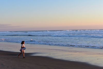 Rear view of woman walking at beach during sunset