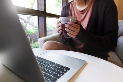 Midsection of woman using mobile phone while sitting on table