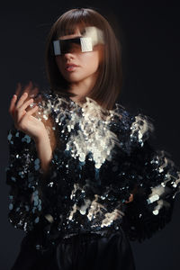 Close-up portrait of young woman standing against black background