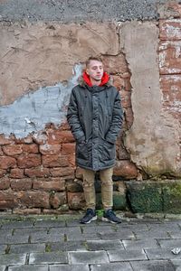 Young man wearing warm clothing standing against brick wall