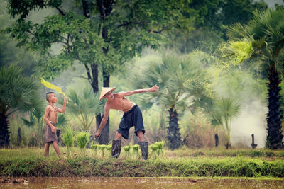 Shirtless mature farmer with grandson working on farm by lake