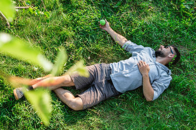 Young handsome sports european man in sunglasses is resting on a grass in summer park, top view.