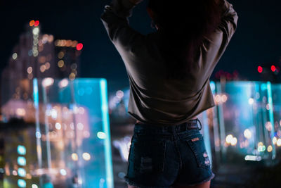 Rear view of woman standing against illuminated city at night