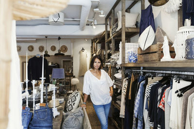 Portrait of confident female owner standing by clothes rack at store