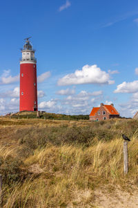 Lighthouse on field by building against sky