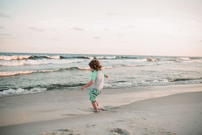 Rear view of boy on beach against sky