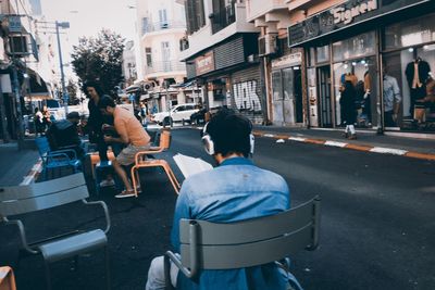 Rear view of people sitting on street against buildings in city