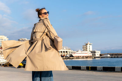 Smiling woman wearing coat standing against sea