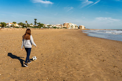 Rear view of woman playing soccer at beach against sky