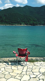 Chair on shore by sea against mountain
