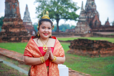 An asian woman in thai dress with hands folded in salutation with ancient ruin temple background