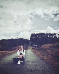 Woman sitting on road against sky