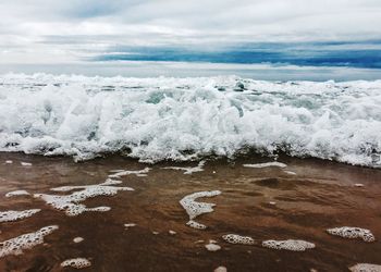 Wave splashing on shore at beach against cloudy sky