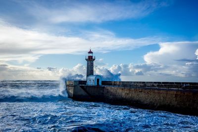 Lighthouse on beach against cloudy sky