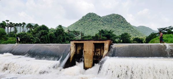 Fisherman crossing over water filled dam