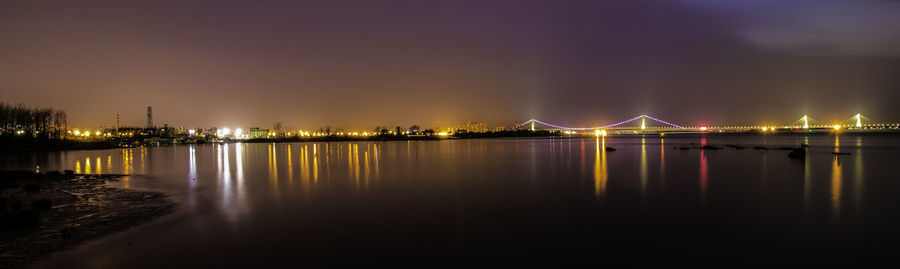 Illuminated city by river against sky at night