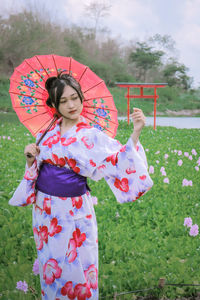 Woman wearing kimono holding pink umbrella while standing in park