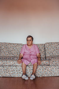 Front view of a senior woman with alzheimer's mental health issues sitting in a sofa alone in her home