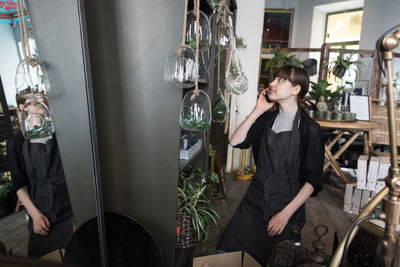 Young female owner talking through mobile phone while kneeling by decorations at store