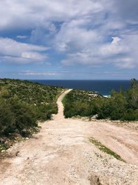 Dirt road leading towards sea against sky