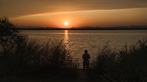 Rear view of silhouette woman walking on beach against sky during sunset