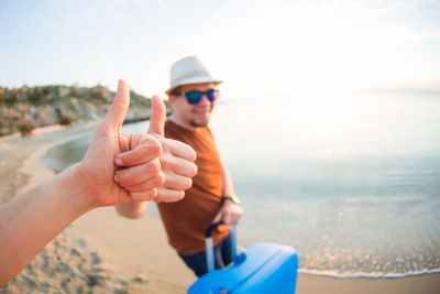 Midsection of man wearing sunglasses at beach against sky