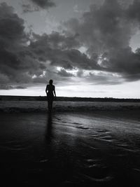 Silhouette man standing on shore against sky