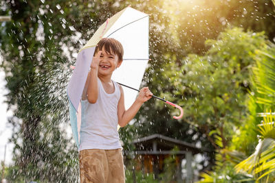 Smiling boy holding umbrella while standing against plants