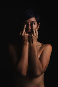 Shirtless mid adult woman showing obscene gesture against black background