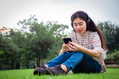 Full length of young man using phone while sitting outdoors