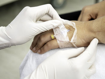Cropped image of doctor removing medical equipment from patient hand in hospital
