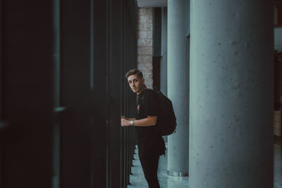 Portrait of young man with backpack standing by window